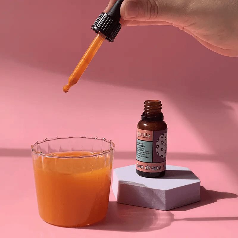 Apelsinų skonio geriamieji įdegio lašai Birdie Nutrition šalia šviežių apelsinų