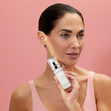 YODEYMA Veido Serumas moters rankose su rožiniu fonu, skirta odos priežiūrai